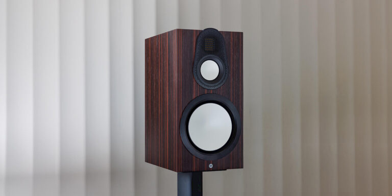 Closeup of the Monitor Audio Gold 100 6G bookshelf speaker in Macassar Wood Veneer finish, placed on a black stand.